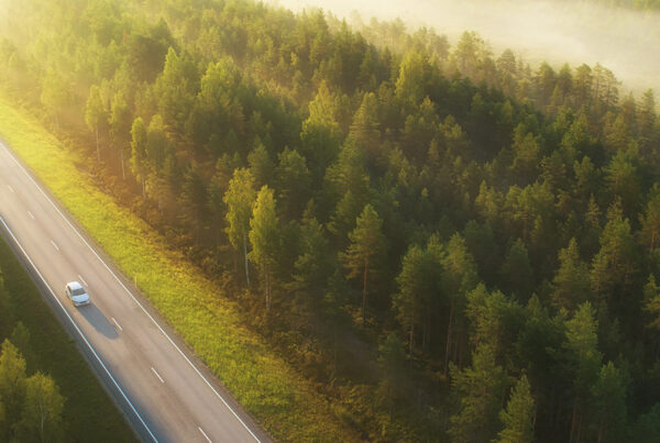 A single car drives down an empty highway in the green forest.